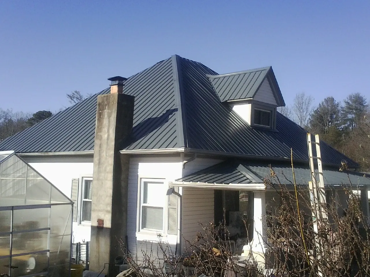 Dark blue standing seam metal roof on a white farmhouse with dormer — Slate & Tile Roof Repair by Roofing Brothers in Coyanosa