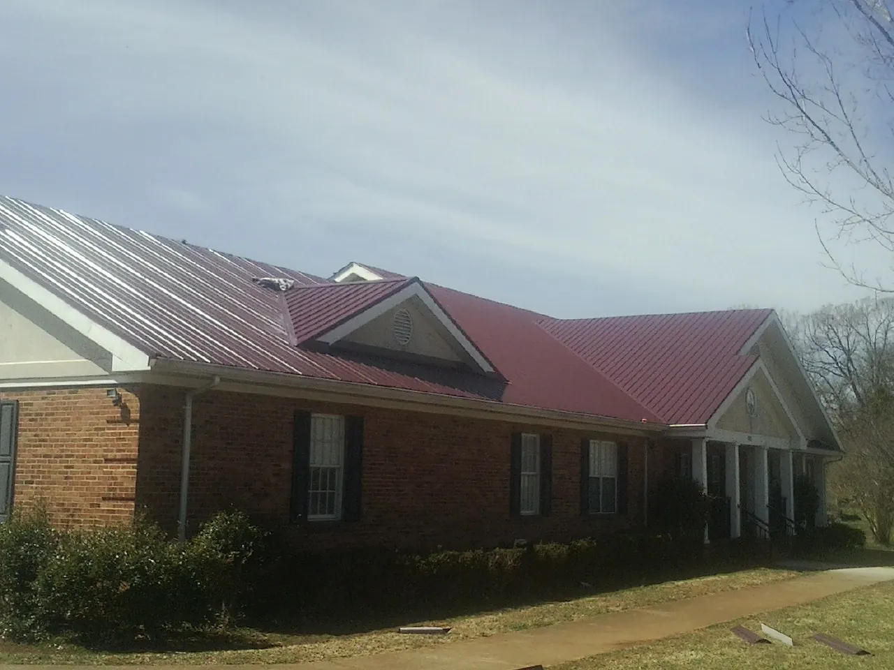 Red metal roof with gabled entries on a long brick building, from a Hail Damage Roof Repair job in Coyanosa