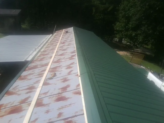 Old rusted panels beside newly installed green metal roofing — Wind Damage Roof Repair by Roofing Brothers in Coyanosa