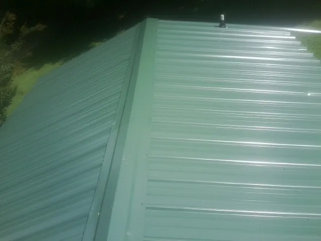 New green metal panels meeting at the ridge of a roof — Flat Roof Repair work by our crew in Coyanosa