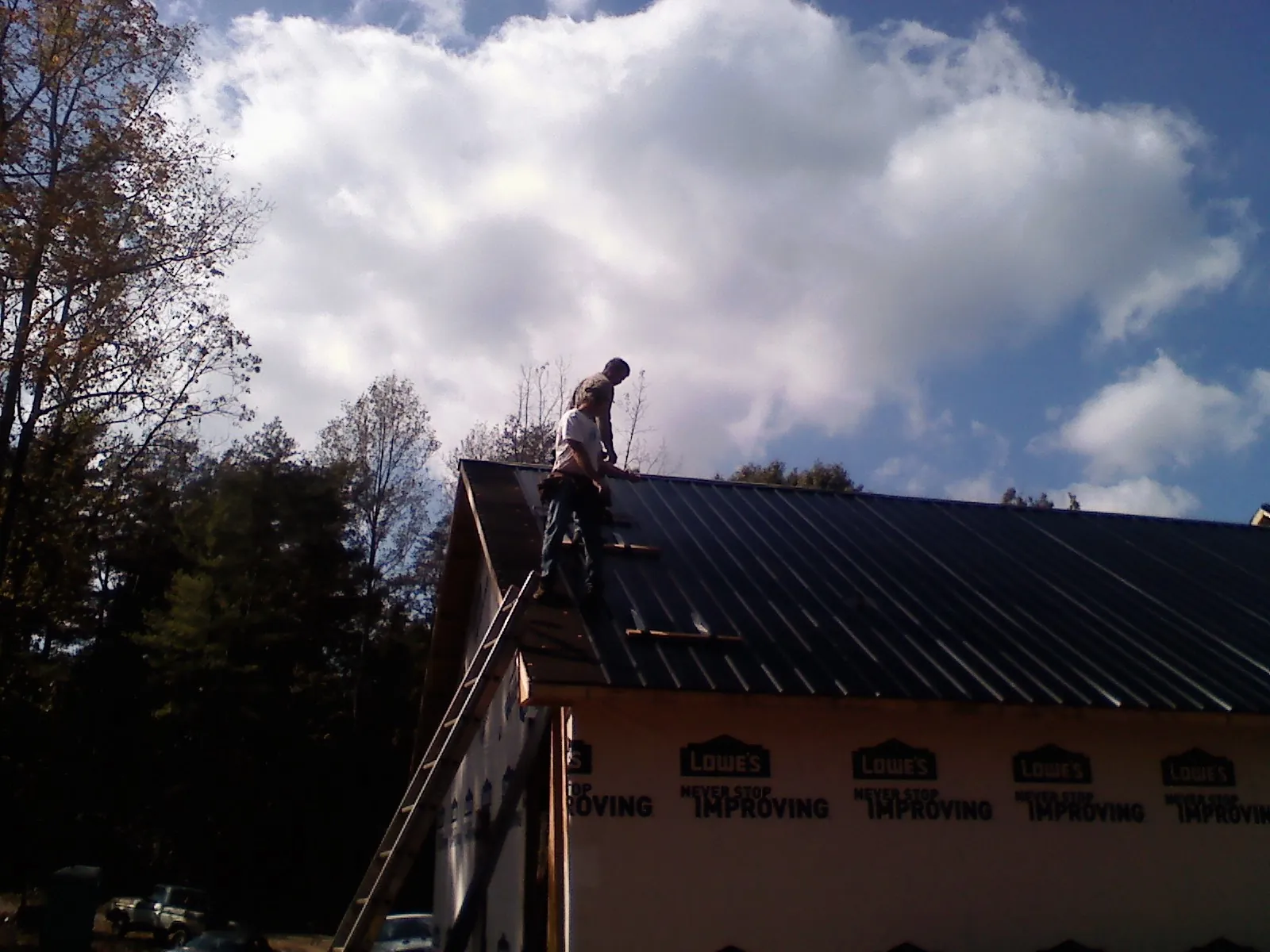 Roofer fastening dark metal panels high against a cloudy sky, from a Roof Inspection job in Coyanosa