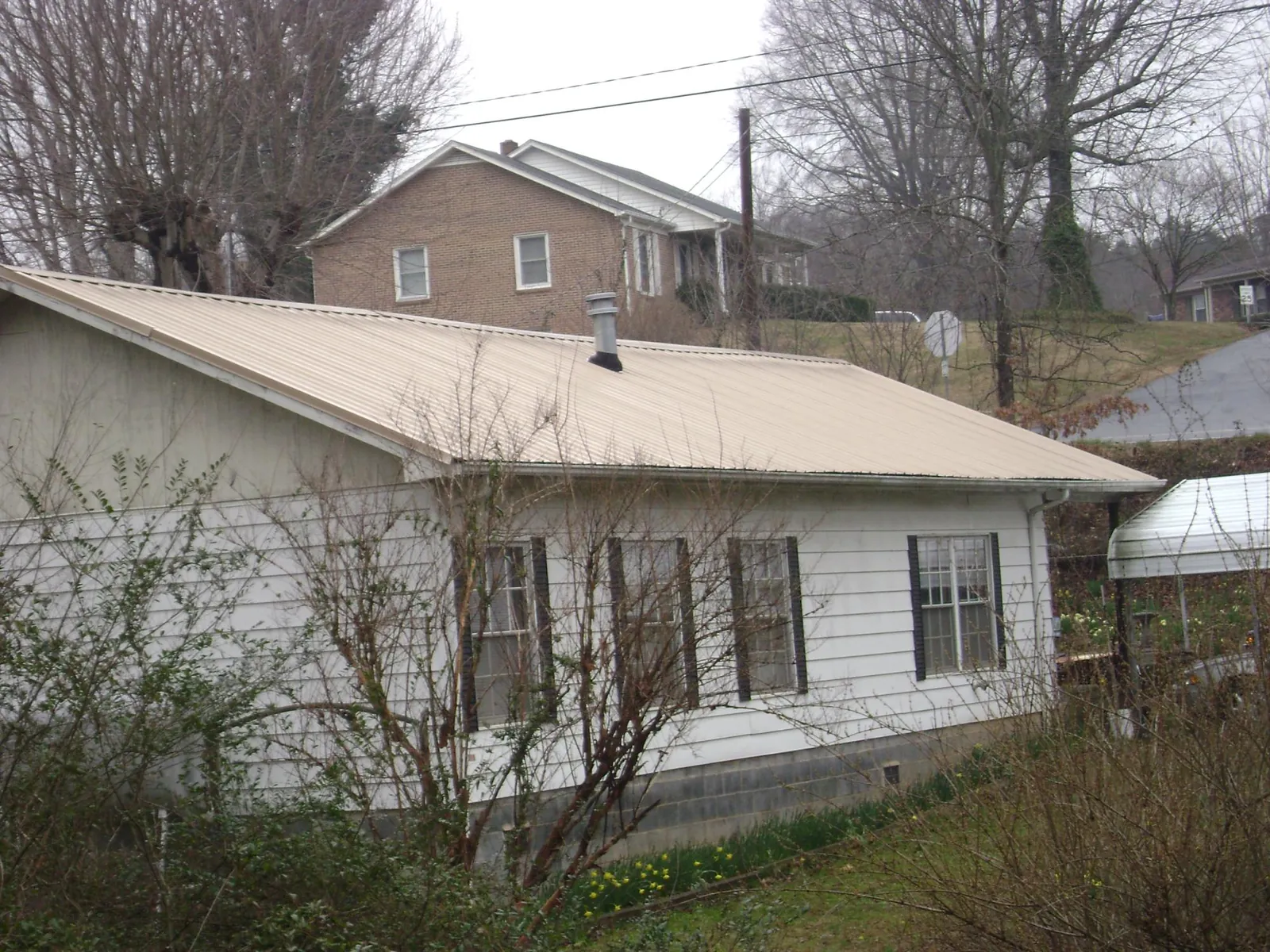 Tan metal roof on a white sided house set into a hillside — Commercial Roofing by Roofing Brothers in Coyanosa
